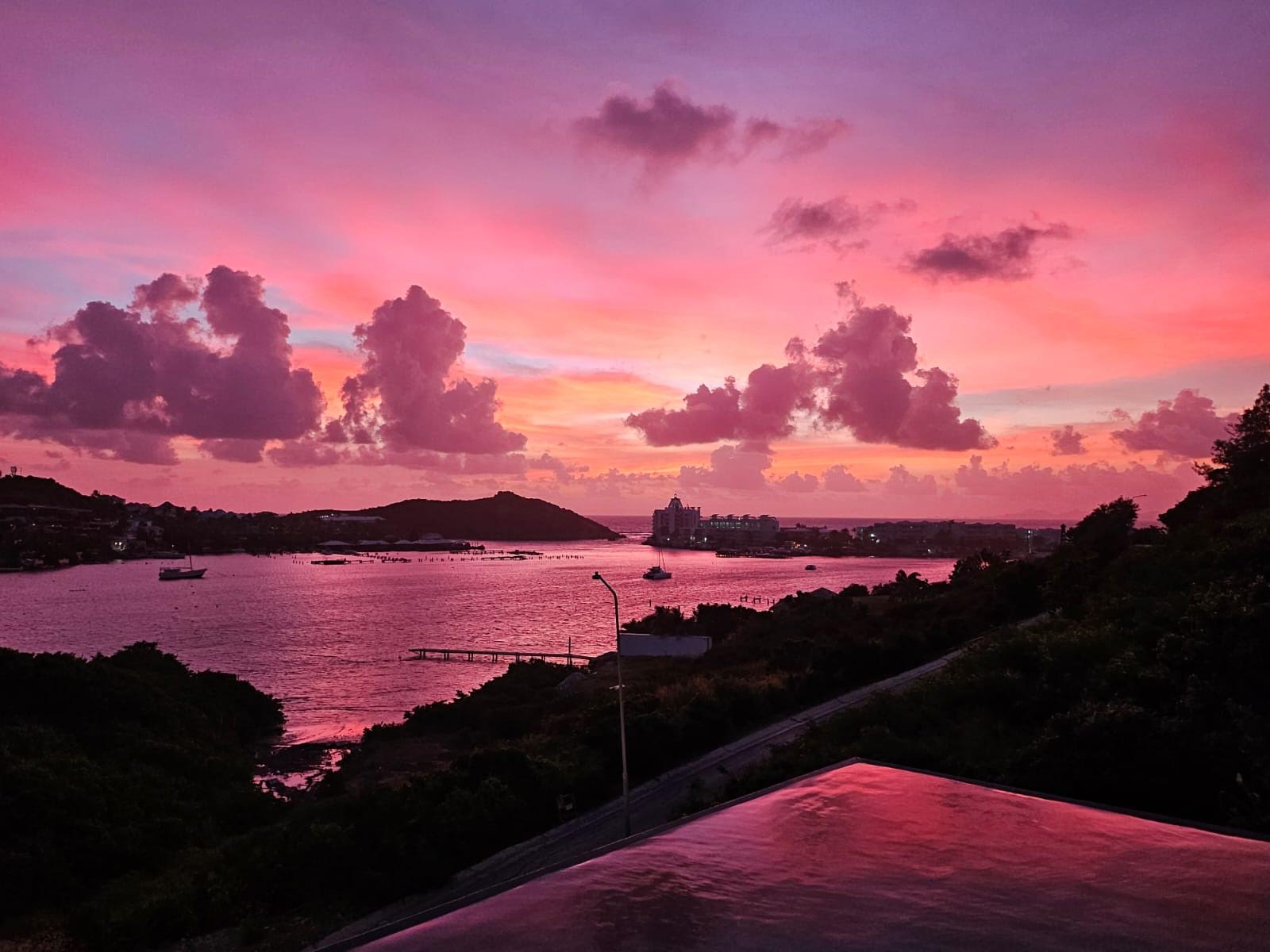A view of a pink sky with grey clouds above the Oyster Pond, during the sunrise on St Maarten
