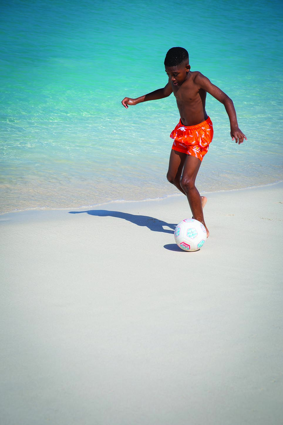 A boy playing soccer on the beach