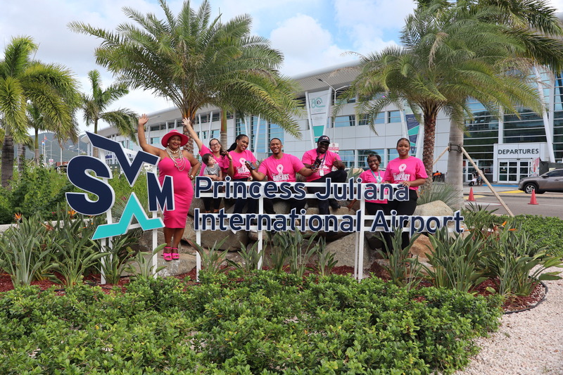 Team of Princess Juliana International Airport infront of the Airport building with breast cancer shirts