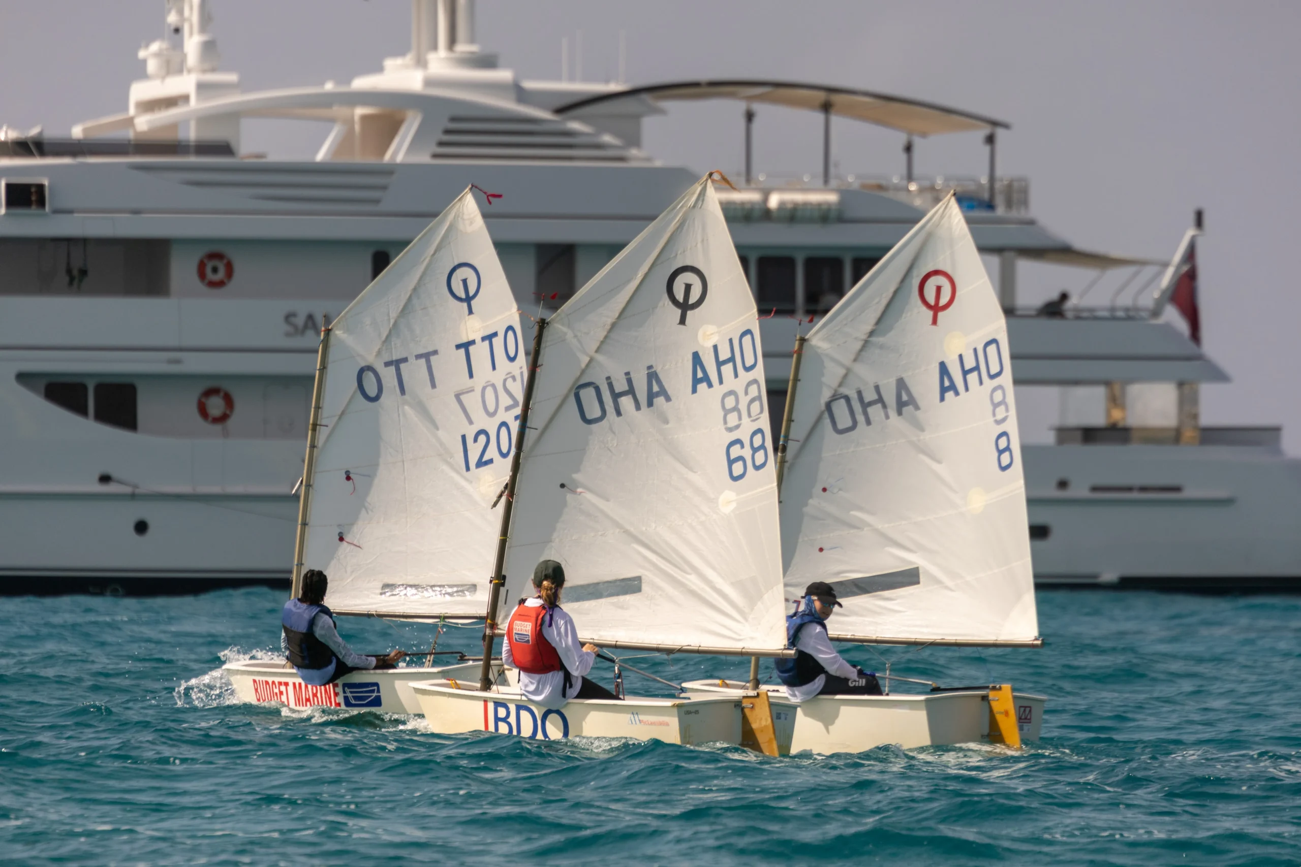 3 boats on the water within the back a big yacht during the Caribbean Dinghy Championship