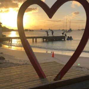 heart statue at the beach where yuou can see the beach and the sunset through